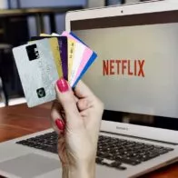 Mano de mujer sosteniendo tarjetas de crédito y Netflix en computador, en nota sobre cómo pagar la 'app' sin ese plástico