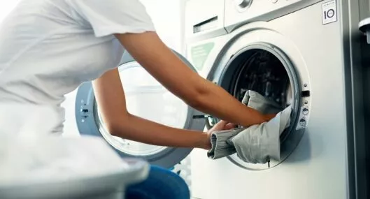 Persona metiendo ropa a la lavandería ilustra nota sobre trucos para que quede sin arrugas