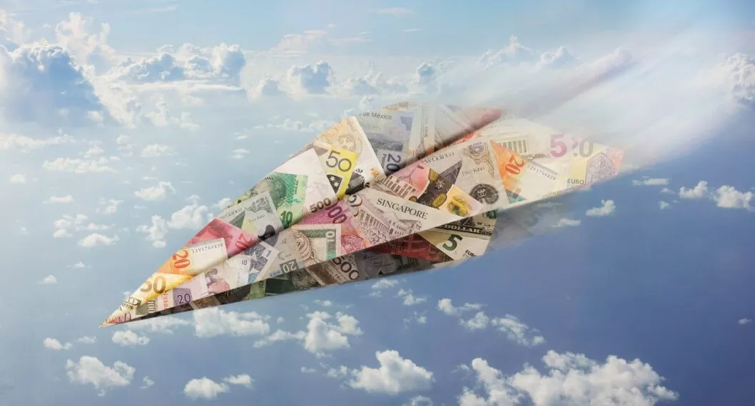Avión de papel con billetes de diferentes países. Nota sobre las monedas de Latinoamérica más afectadas por el alza del dólar.