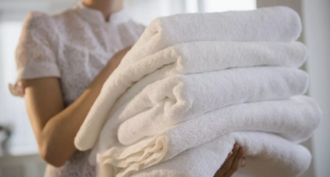 Mujer cargando toallas ilustra nota sobre trucos para que queden suaves y con buen aroma