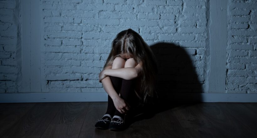 Sad desperate young girl suffering from bulling and harassment felling lonely, unhappy desperate and hopeless sitting against the wall, dark light. School isolation, abuse and bullying concept
