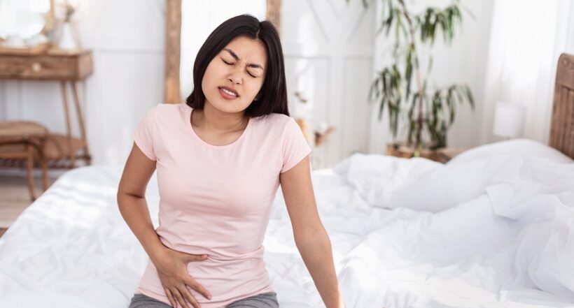 Menstrual Cramps. Chinese Girl Having Pelvic Lower Abdominal Pain Having Reproductive Health Problem Sitting In Bed At Home. Copy Space