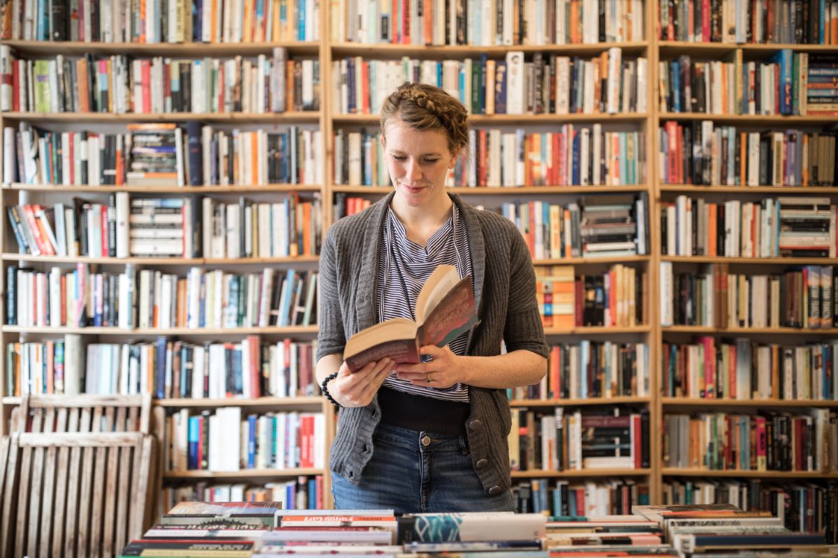 Mujer en frente de un estante de libros leyendo ilustra nota sobre los mejores de la historia, según ChatGPT.
