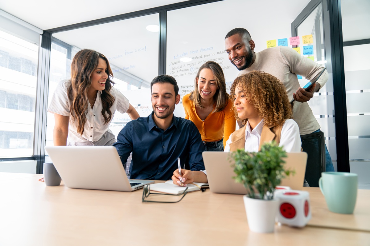 Happy group of Latin American coworkers sharing ideas in a business meeting and smiling while using a laptop