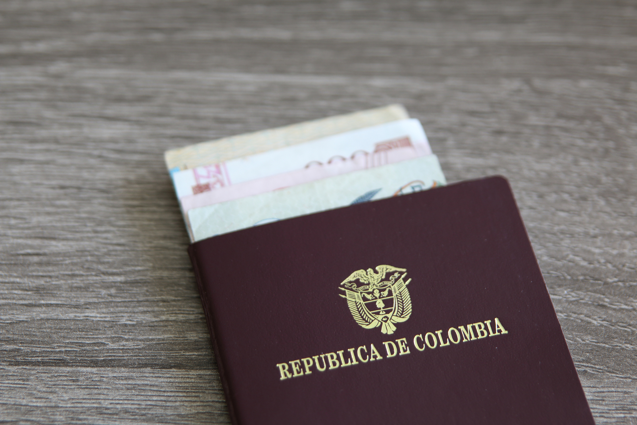 Colombian passport with bank notes over a light grey wooden background