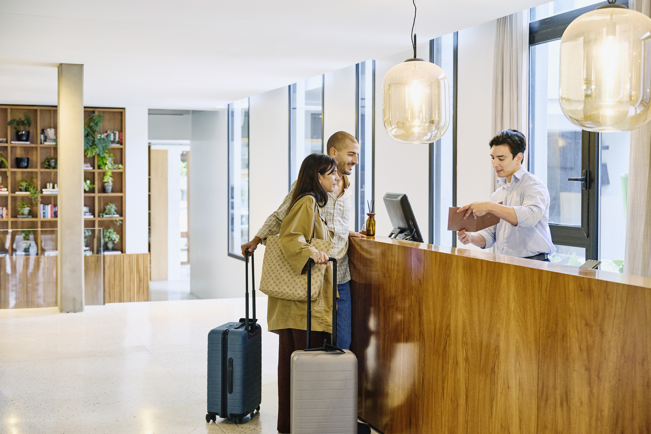 Wide shot of male concierge explaining hotel information and giving room key to guests at lobby reception desk during checking in