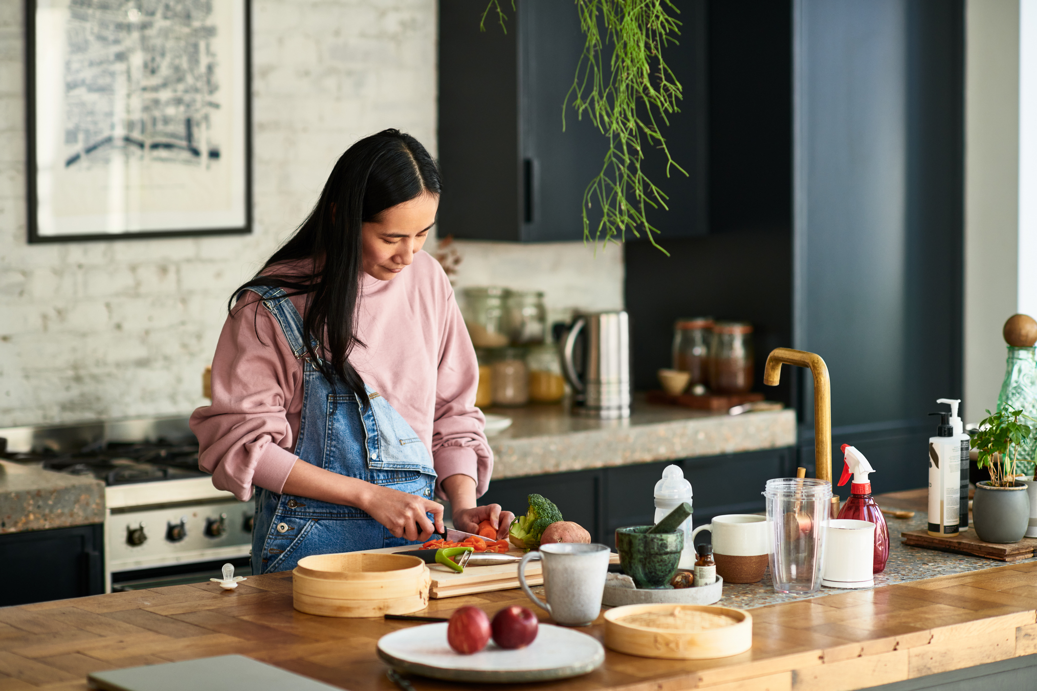 Mid adult woman chopping ingredients for meal, standing behind kitchen worktop, concentration, precision, cutting