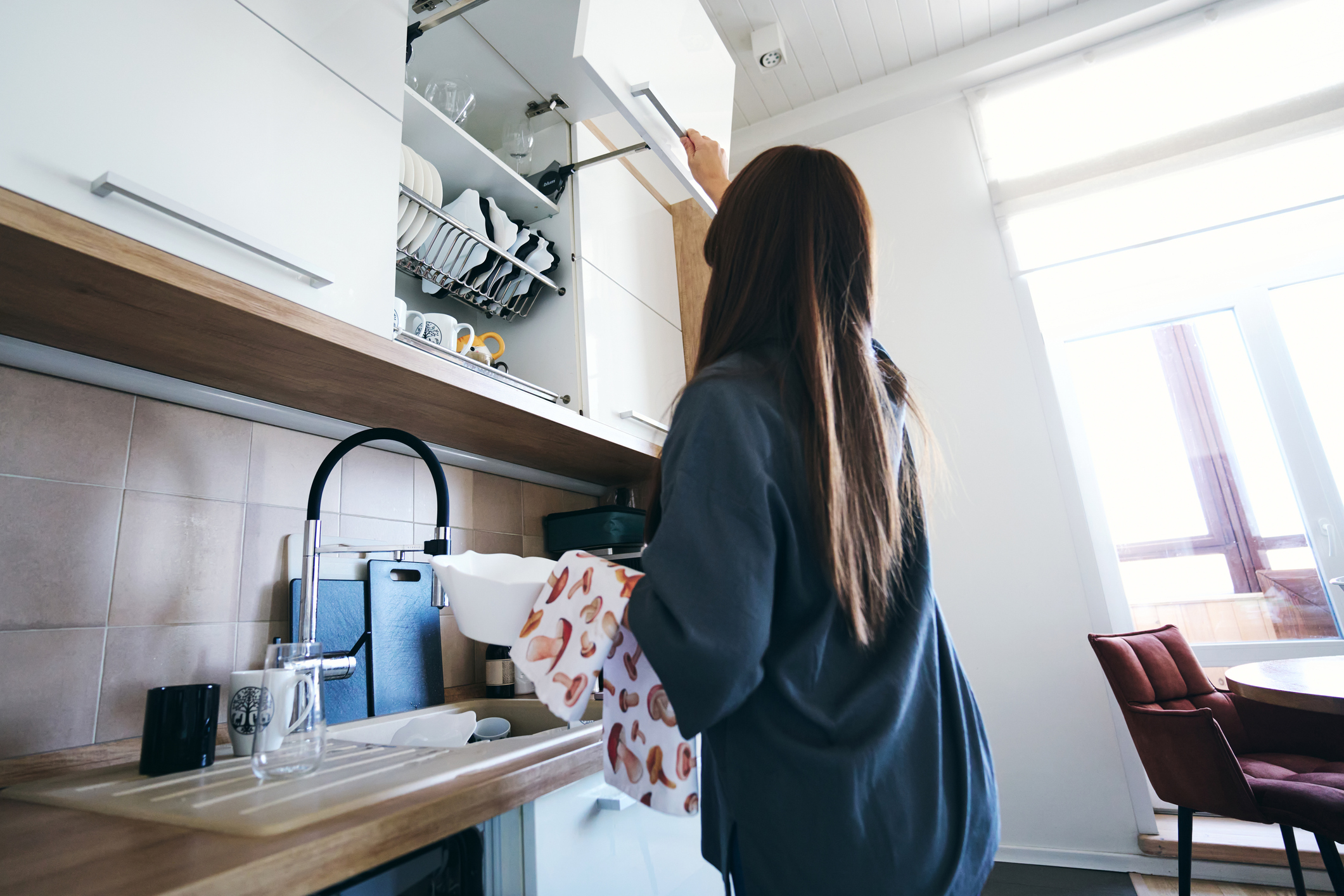 Woman putting away clean dishes into a kitchen cabinet, engaging in daily household chores and maintaining a tidy home