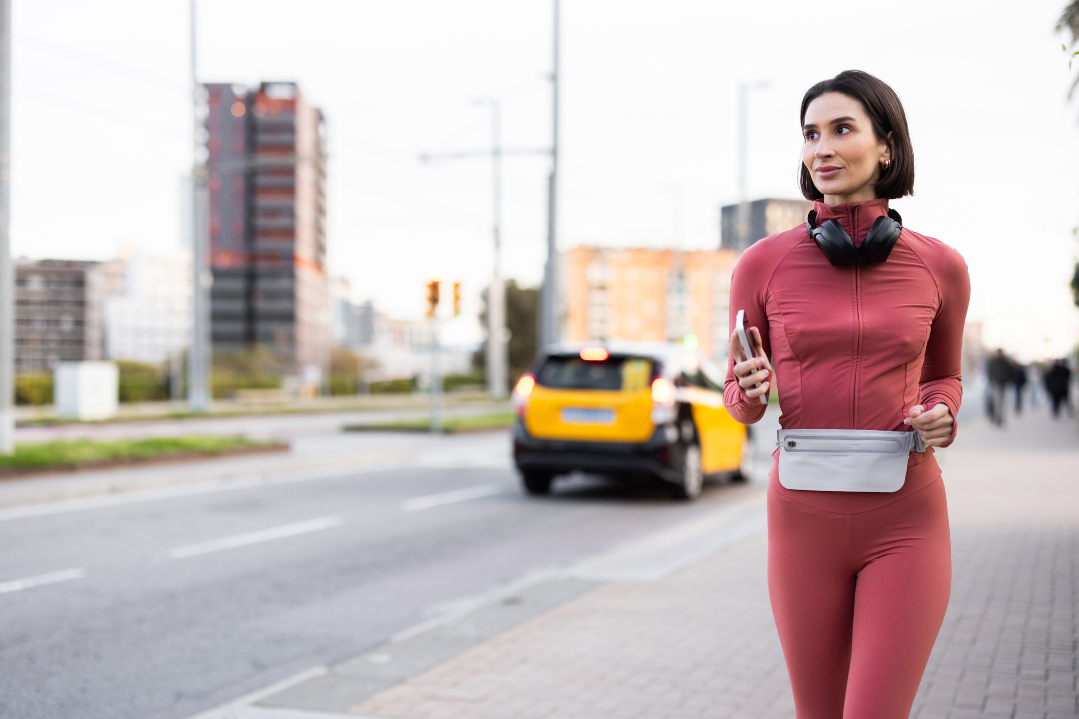 Woman jogging on a city street, carrying a smartphone and wearing headphones