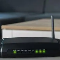 Router de internet con un computador al fondo ilustra nota sobre la altura de este objeto para mejorar la señal de wifi.