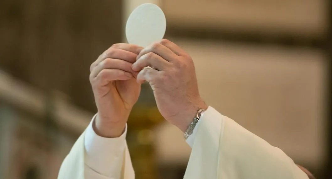 Padre católico elevando sus manos a propósito del origen del Jueves Santo.