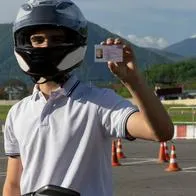 Hombre con casco de moto sostiene licencia de conducción ilustra nota sobre renovación de este documento.