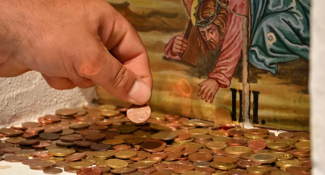 Foto de un hombre tomando una moneda, con una imagen de Cristo al frente, para ilustrar artículo sobre robo a una iglesia en Antioquia.
