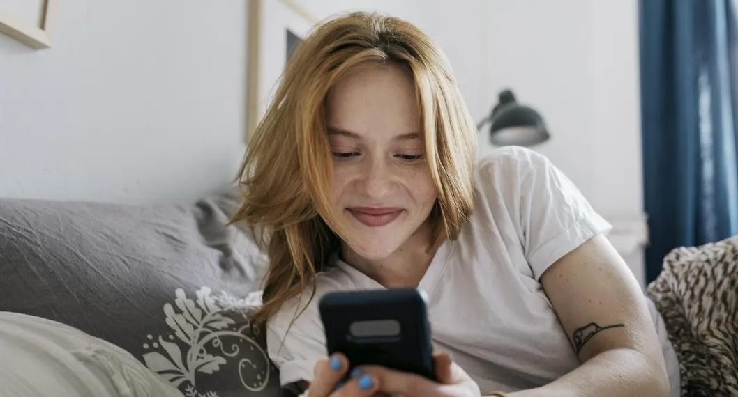 Mujer feliz en su celular a propósito de cómo recuperar los mensajes eliminados en WhatsApp.