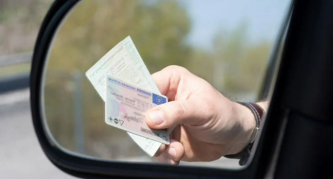 Espejo retrovisor de un vehículos muestra documentos ilustra nota sobre la licencia de conducción.