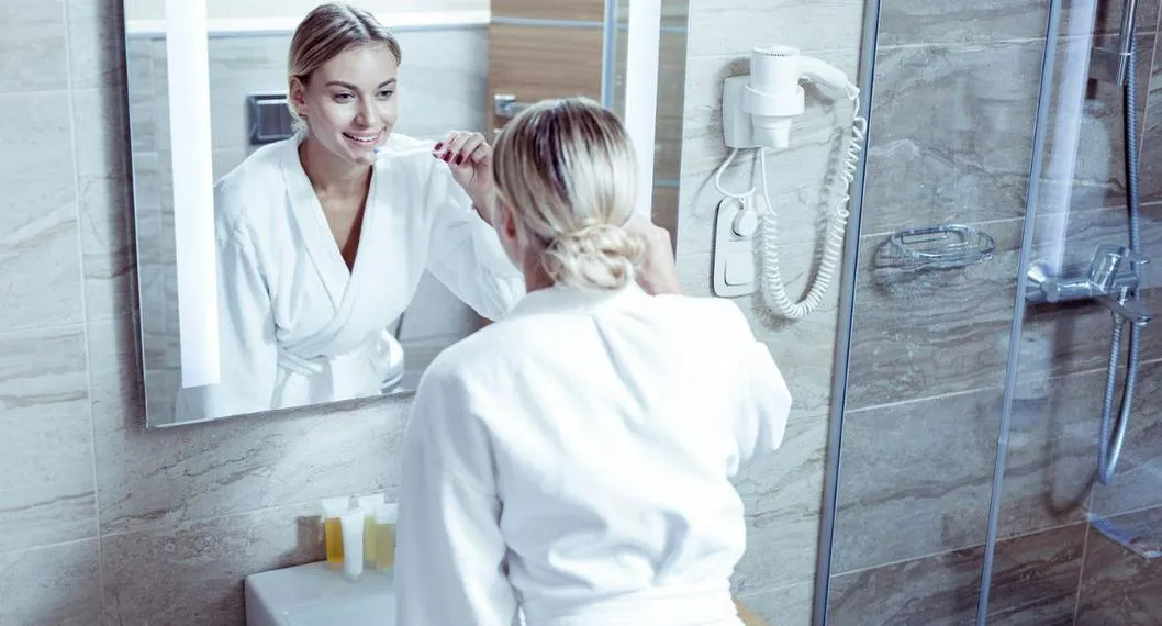 Persona cepillándose a propósito de cómo eliminar las manchas de crema dental que quedan en el espejo.