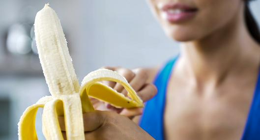 Mujer comiendo plátano en nota sobre qué son las hebras blancas y si se pueden consumir