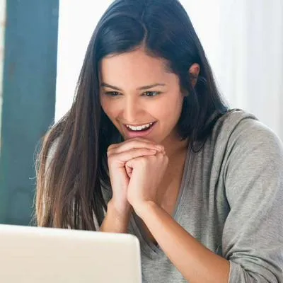 Foto mujer contenta frente a computador, en nota de que Colpensiones explicó cómo ayuda caja de compensación en Colombia a pensionados