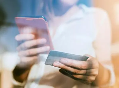 Mujer con celular y tarjeta de crédito. En relación con tips para cancelar  la tarjeta.