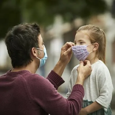 Padre poniendo tapabocas a su hija. Estudio indica que la exposición a aire contaminado afecta su cerebro.