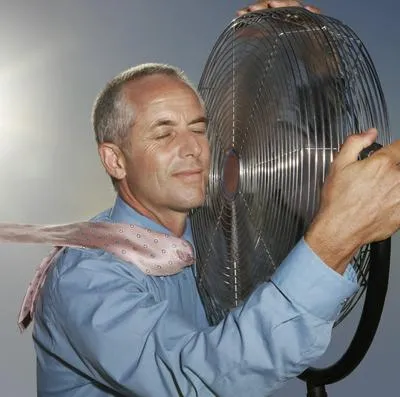 Hombre abrazando ventilador por ola de calor, que sería mortal para los humanos.