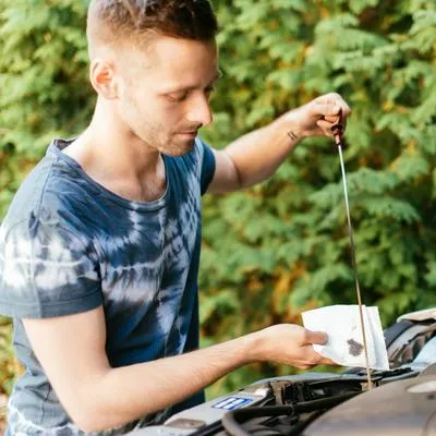 Hombre revisando el nivel de aceite de su carro, como las recomendaciones que se entregan.