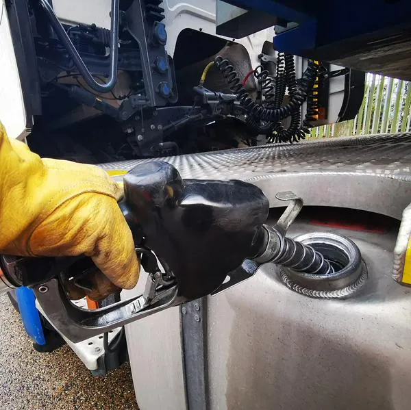 Semi Truck Being Refuelled with Diesel Close up with the Gloved Hand of the Truck Driver Holding the Fuel Nozzle and holding it in Place as He Fills up the Tank.