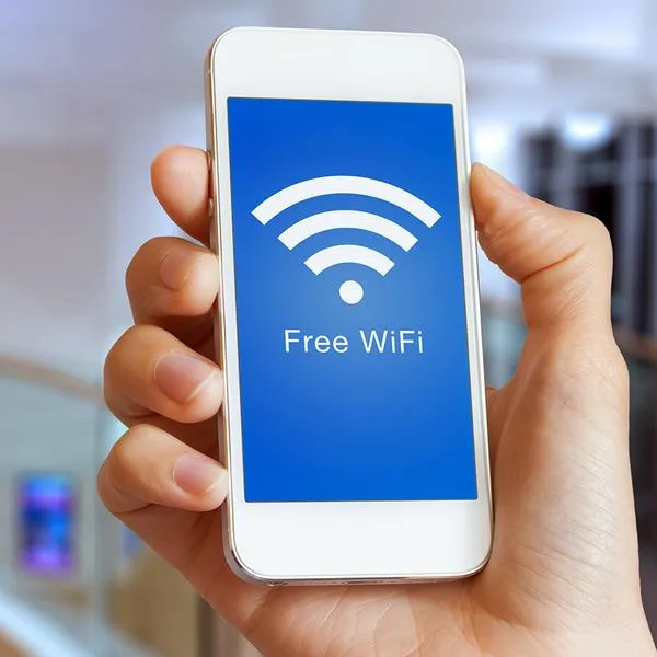 Close-up of hand holding smartphone with free WiFi hotspot icon on the screen to connect to wireless internet, public building interior in background