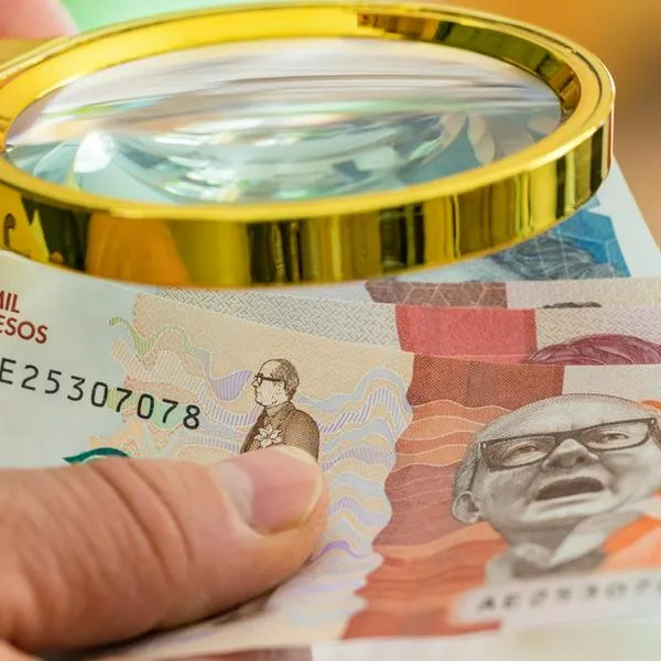 Colombian money held in the hand and viewed through a lupe, business and economic concept