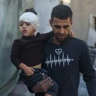 Hombre palestino huye del lugar de un bombardeo con un niño en la Franja de Gaza.