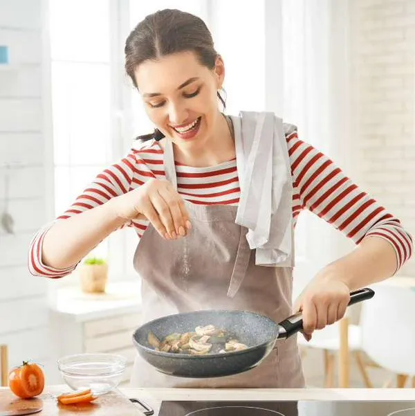 Foto de mujer cocinando, en nota de cómo evitar que la pared de la cocina se llene de grasa con pasos fáciles en casa