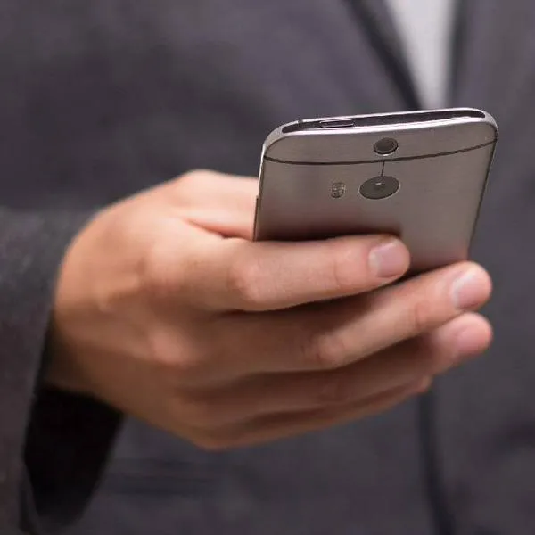 Foto de persona con dispositivo móvil, en nota de qué es más seguro entre huella digital o reconocimiento facial para el celular