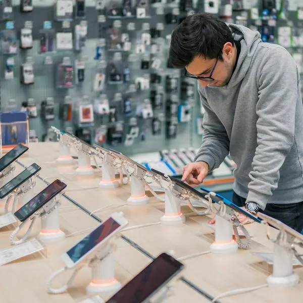 Hombre mirando celulares en supermercado, en nota sobre el que abrirá dos nuevas tiendas 