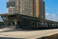 Passengers at a Transmilenio bus stop on an avenue with apartment buildings in the background. Bogota. Colombia. August 30, 2024.