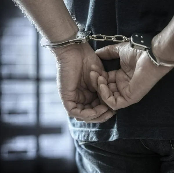 Arrested man in handcuffs with handcuffed hands behind back in prison