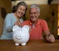 Happy senior couple at home saving money in a piggy bank and smiling - home fincances concepts