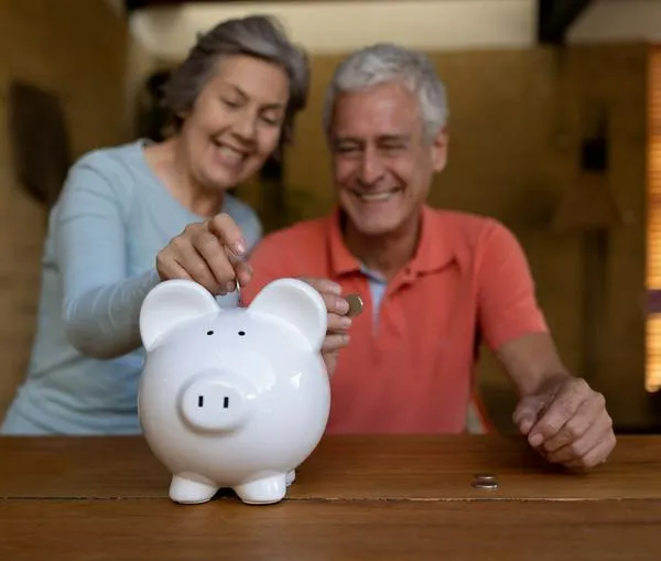 Happy senior couple at home saving money in a piggy bank and smiling - home fincances concepts