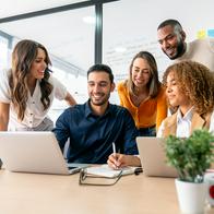 Happy group of Latin American coworkers sharing ideas in a business meeting and smiling while using a laptop