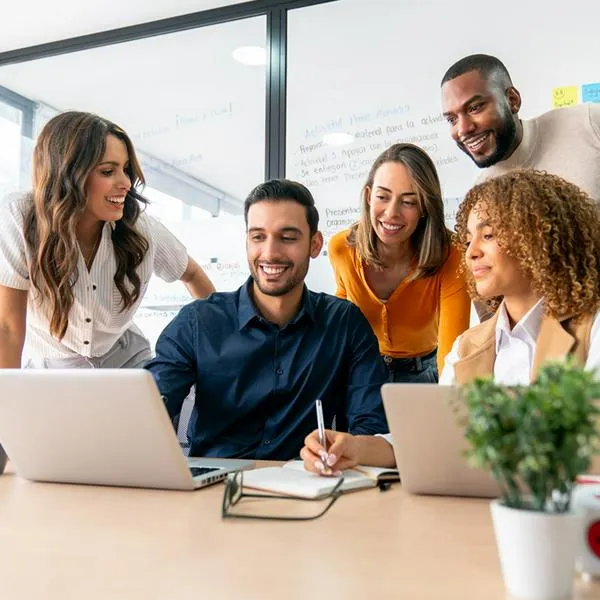 Happy group of Latin American coworkers sharing ideas in a business meeting and smiling while using a laptop