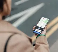 Over the shoulder view of young woman using smartphone to arrange taxi service in the city. Concept of transport and technology.