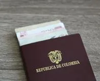 Colombian passport with bank notes over a light grey wooden background