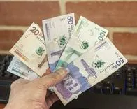 A man holds several Colombian peso bills in his hand.