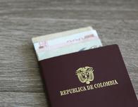 Colombian passport with bank notes over a light grey wooden background
