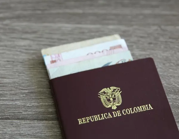 Colombian passport with bank notes over a light grey wooden background