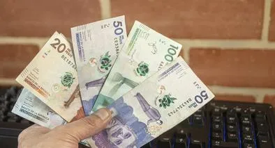 A man holds several Colombian peso bills in his hand.