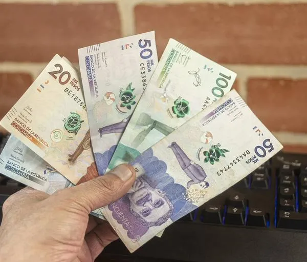 A man holds several Colombian peso bills in his hand.