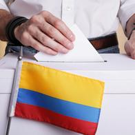 A man inserting a ballot to a ballot box.  Colombian flag in front of it.