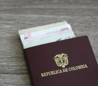 Colombian passport with bank notes over a light grey wooden background