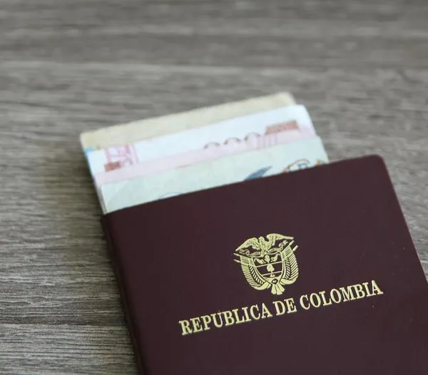 Colombian passport with bank notes over a light grey wooden background