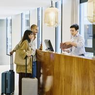 Wide shot of male concierge explaining hotel information and giving room key to guests at lobby reception desk during checking in
